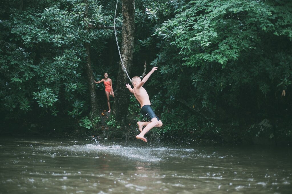 Children swinging from rope into creek