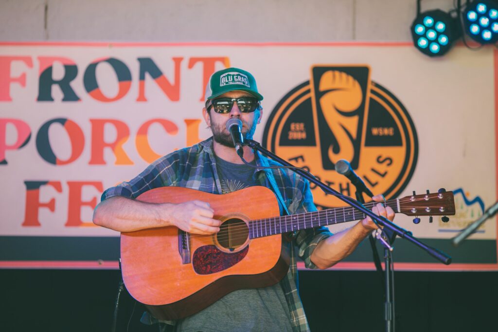 Man on stage with guitar, with Front Porch Fest sign in background